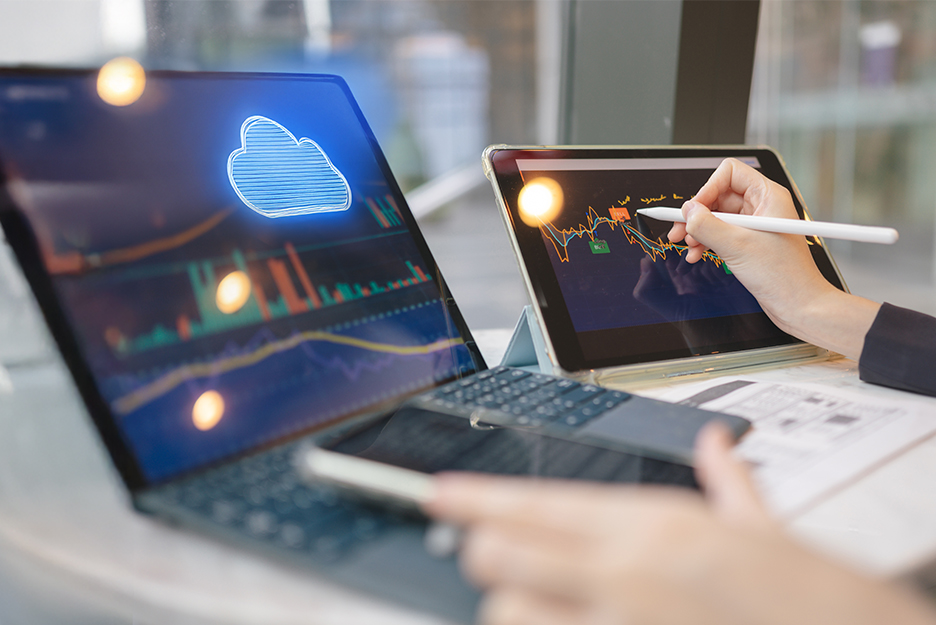 Laptop und Tablet mit Cloud-Symbol und Finanzdiagrammen, Hand zeichnet mit Eingabestift eine Kurve auf dem Bildschirm.