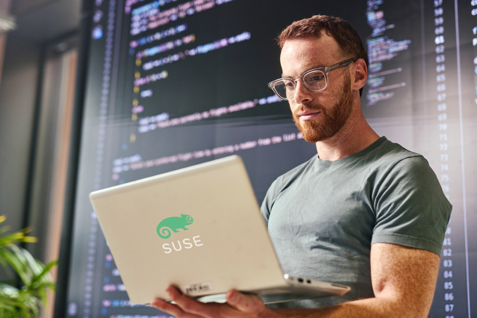 Ein IT-Experte arbeitet mit Laptop und dem SUSE Betriebssystem IT-Experte arbeitet an einem Laptop vor Code-Anzeigen auf Bildschirmen. Das Bild steht für ein modernes Cloud-Betriebssystem-Upgrade mit SUSE Linux.