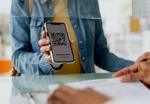 Eine Frau zeigt einem Mitarbeitendem einer Behörde ihr Smartphone mit einem QR-Code