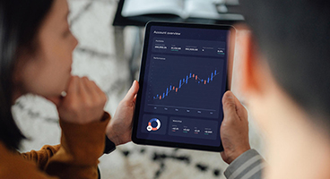 Eine Frau und ein Mann halten ein Tablet auf dem eine Auswertung zu sehen ist. 